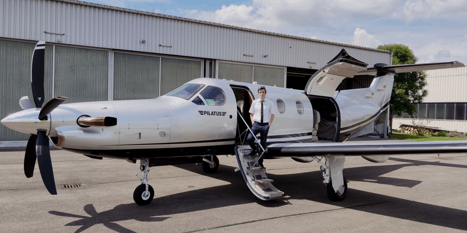 Tim Hittinger standing on the airstair of a Pilatus PC-12 in front of a hangar.